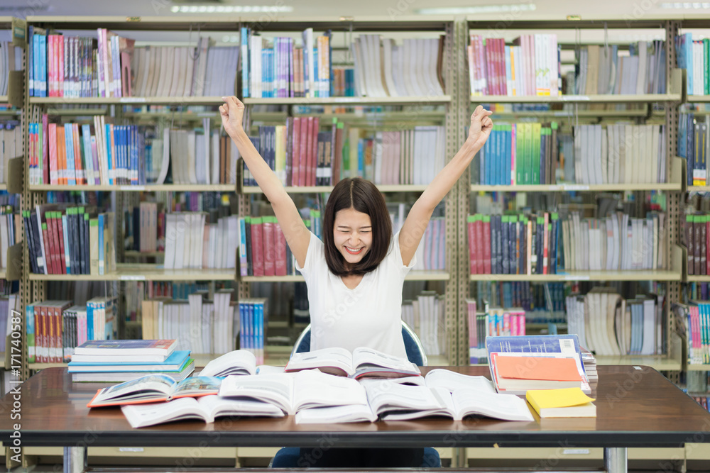 年轻的亚洲快乐女学生在图书馆举起双手庆祝阅读考试结束