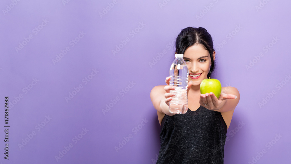 Happy young woman holding an apple and a water bottle