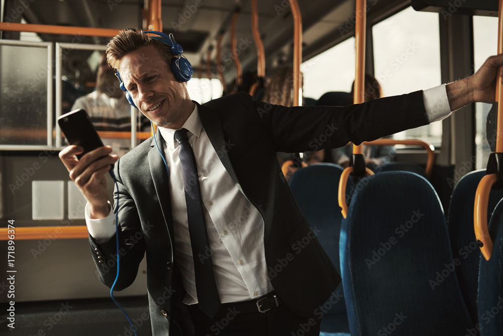 Smiling businessman standing on a bus listening to music