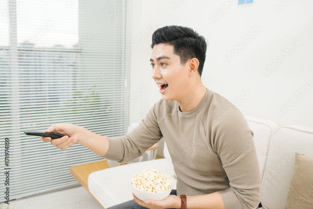 Young man eating popcorn and watching movies relaxed on couch at home