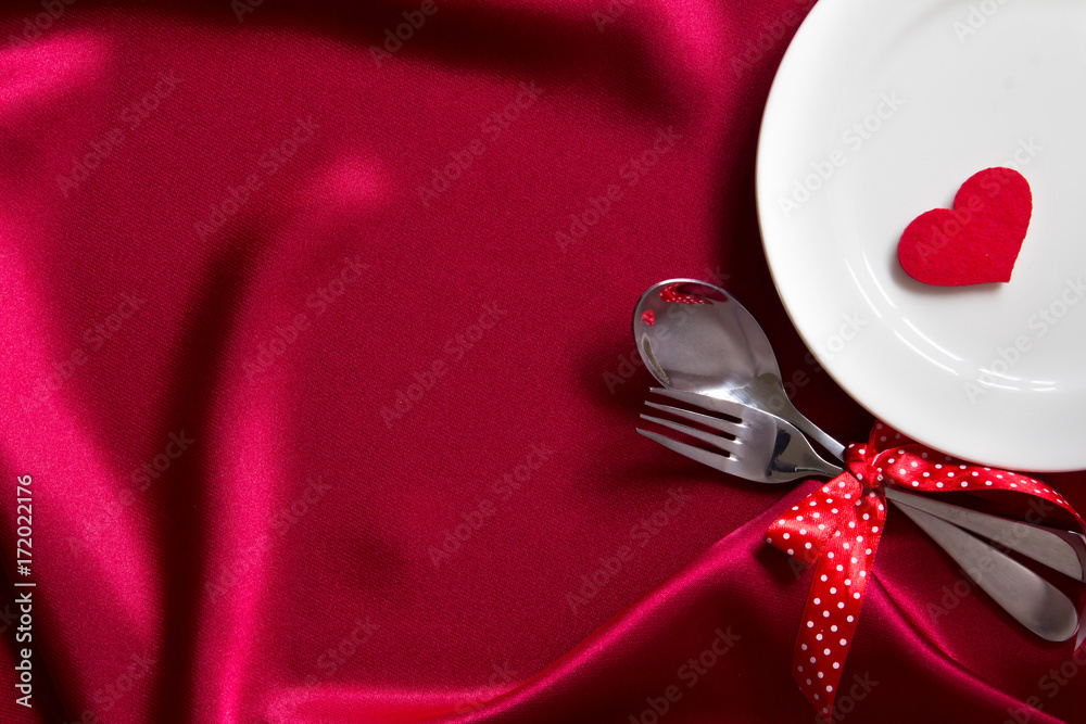 red heart shape with White empty plate with fork and spoon on red silk fabric for love dinner concep