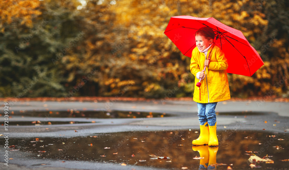 happy child girl with an umbrella and rubber boots in puddle  on autumn walk