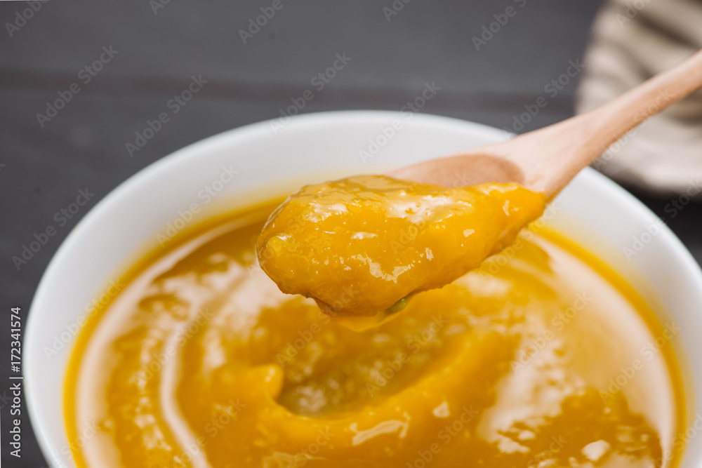 Spoon of homemade pumpkin soup on blank stone background.