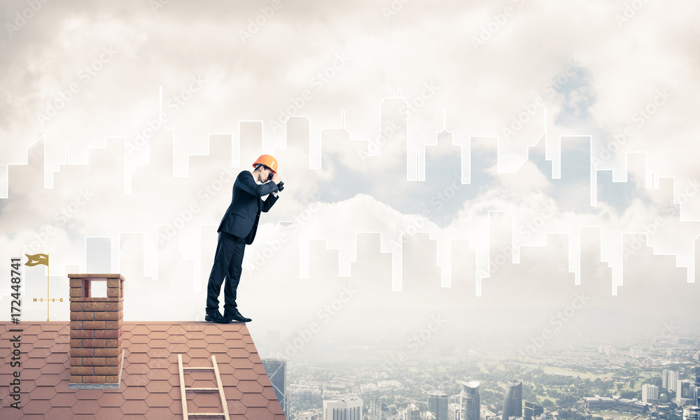 Engineer man standing on roof and looking in binoculars. Mixed m