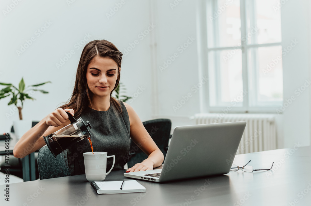 女人的手把咖啡倒进办公桌上的玻璃杯中。