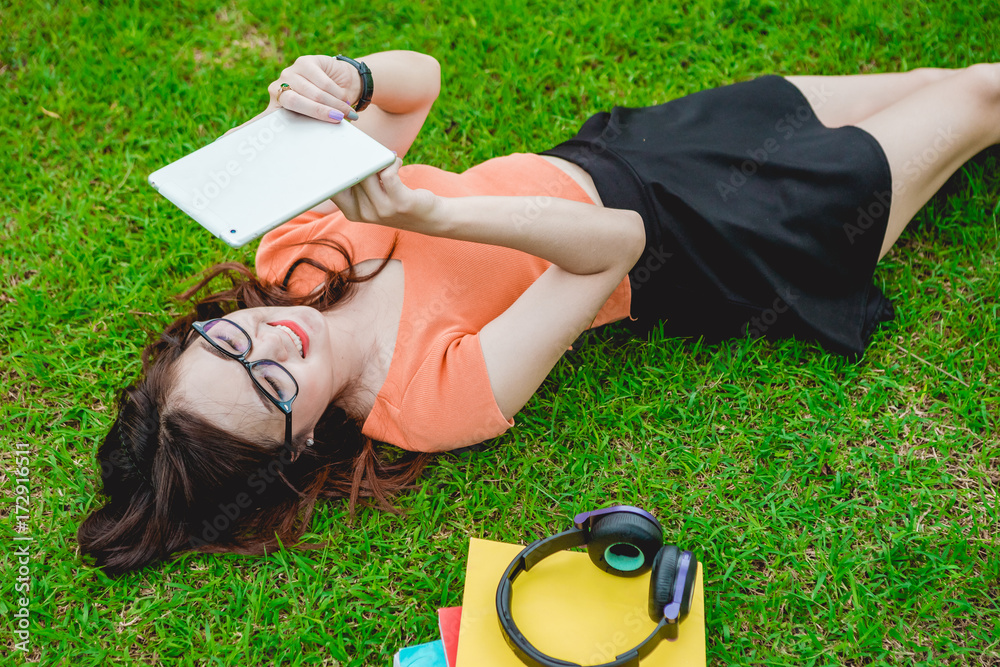 Asian teenage girls sit and relax use tablet to play the Internet to play in the park on weekends.