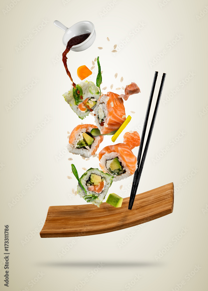 Flying sushi pieces served on wooden plate, separated on soft background