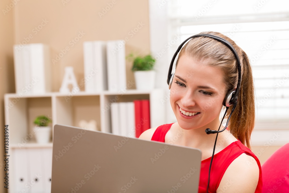 Happy young woman using her laptop and headset at home