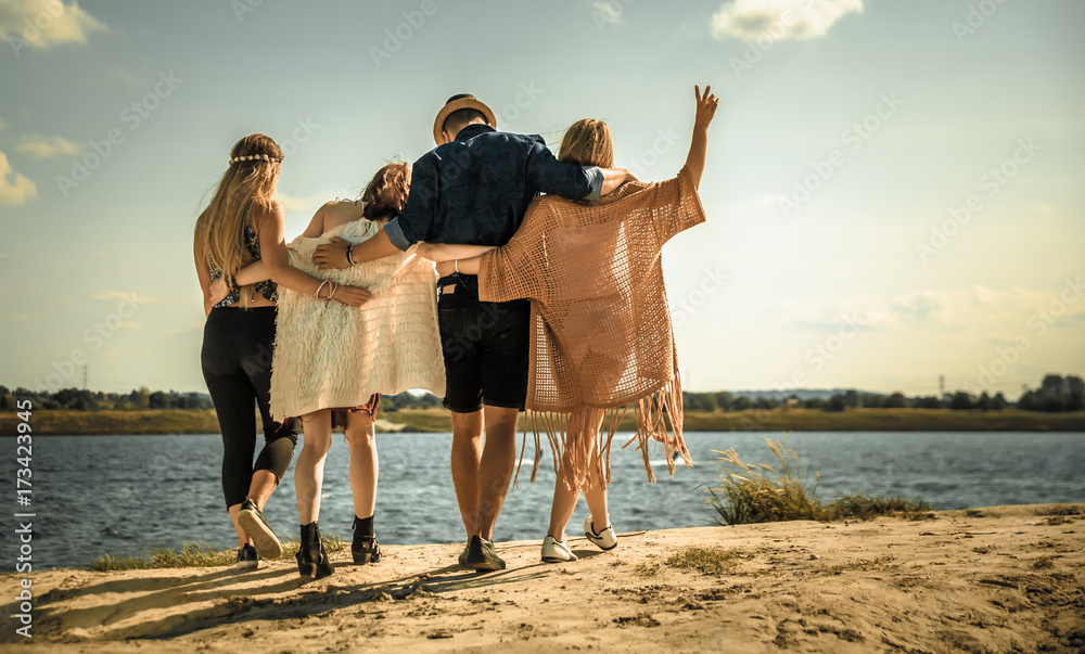 Group of happy friends walking on beach, fashion styled