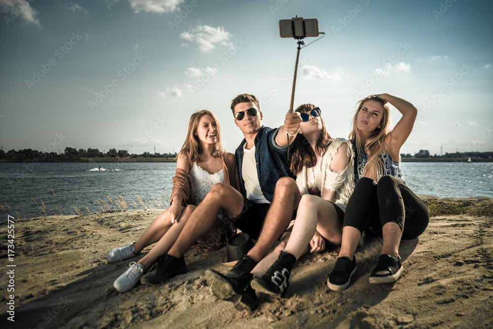 Group of friends taking self portrait with selfie stick, having fun at beach