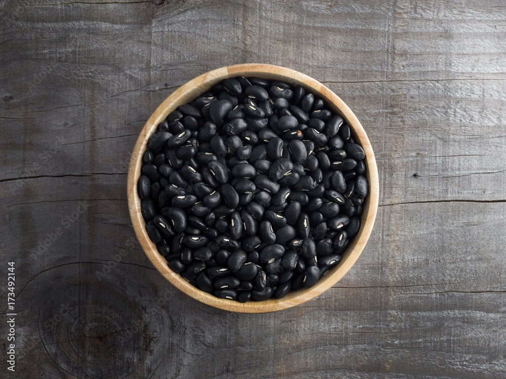 Black beans in a wooden bowl, black beans in a wooden spoon on a wood background