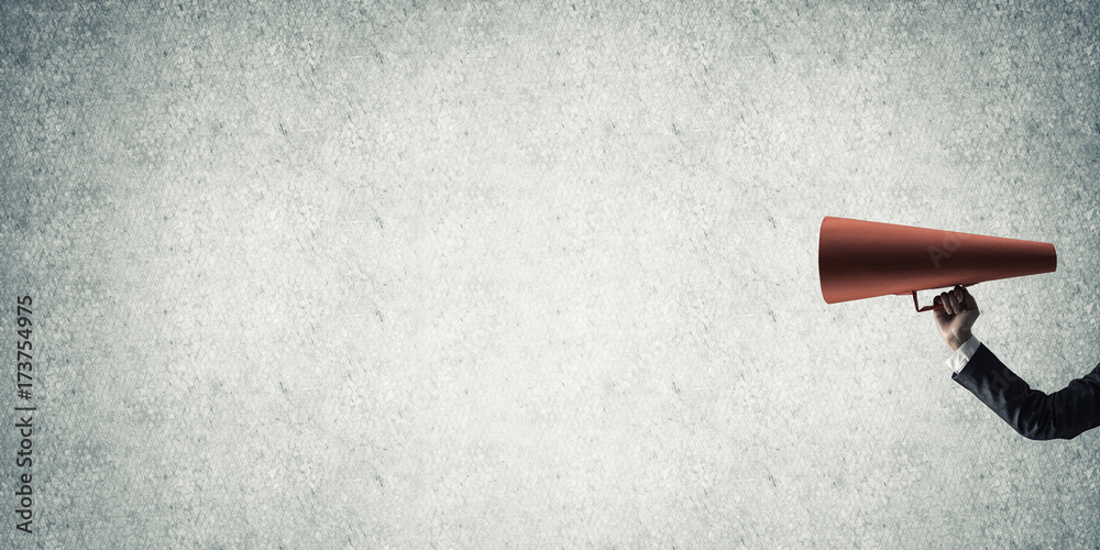 Hand of businesswoman holding red paper trumpet against concrete background