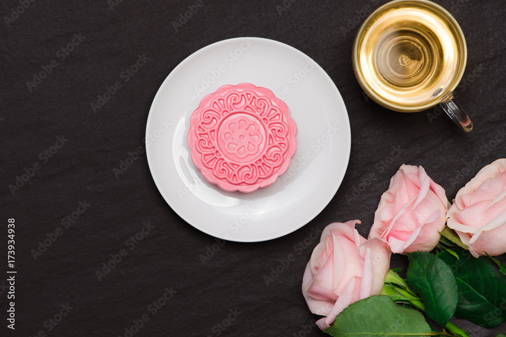 Sweet color of snow skin mooncake and tea cup with flowers on dark background.