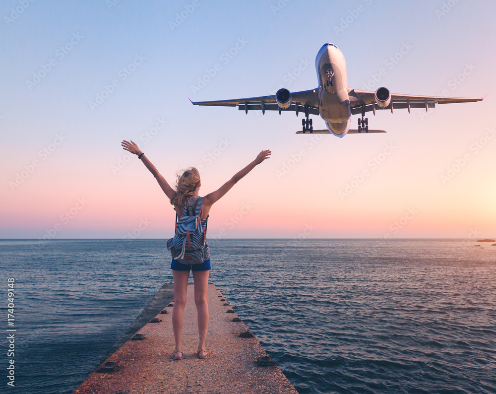 Airplane and woman at sunset. Summer landscape with girl standing on the sea pier with raised up arm