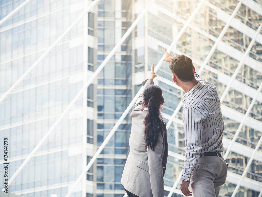 two of young caucasian businessman businesswoman 20-30s standing in the modern city, pointing out sh