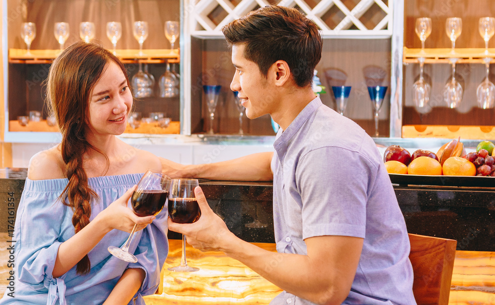 Teen Asian couple drinking wine in front of the bar to drink in their home to celebrate Valentines 