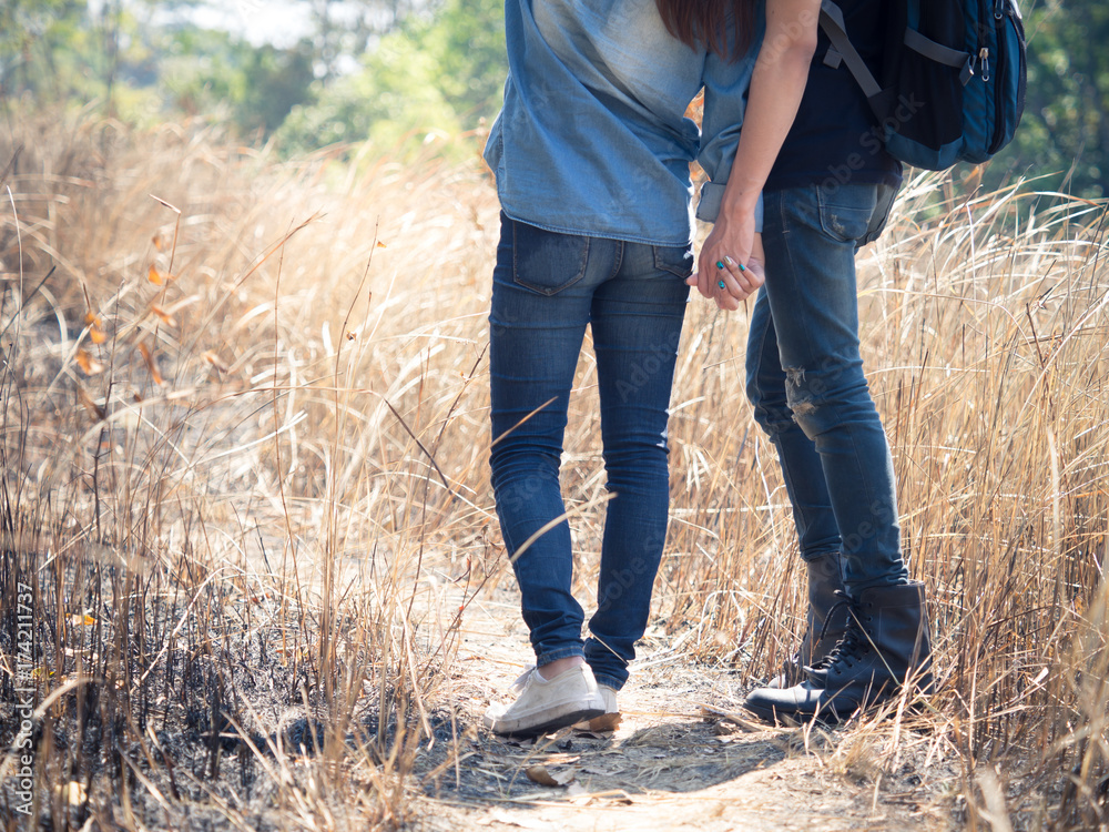 Two young couple wears jeans holding hands in meadow, hipster looking, walking to travel in mountain