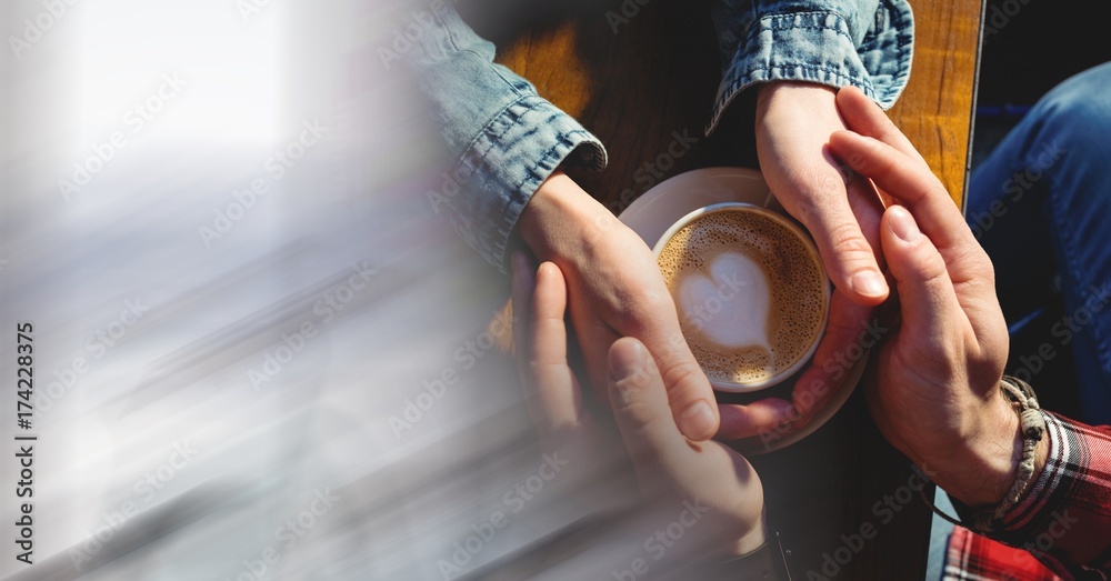 Overhead of two pairs of hands around coffee cup with heart in foam with blurry white transition