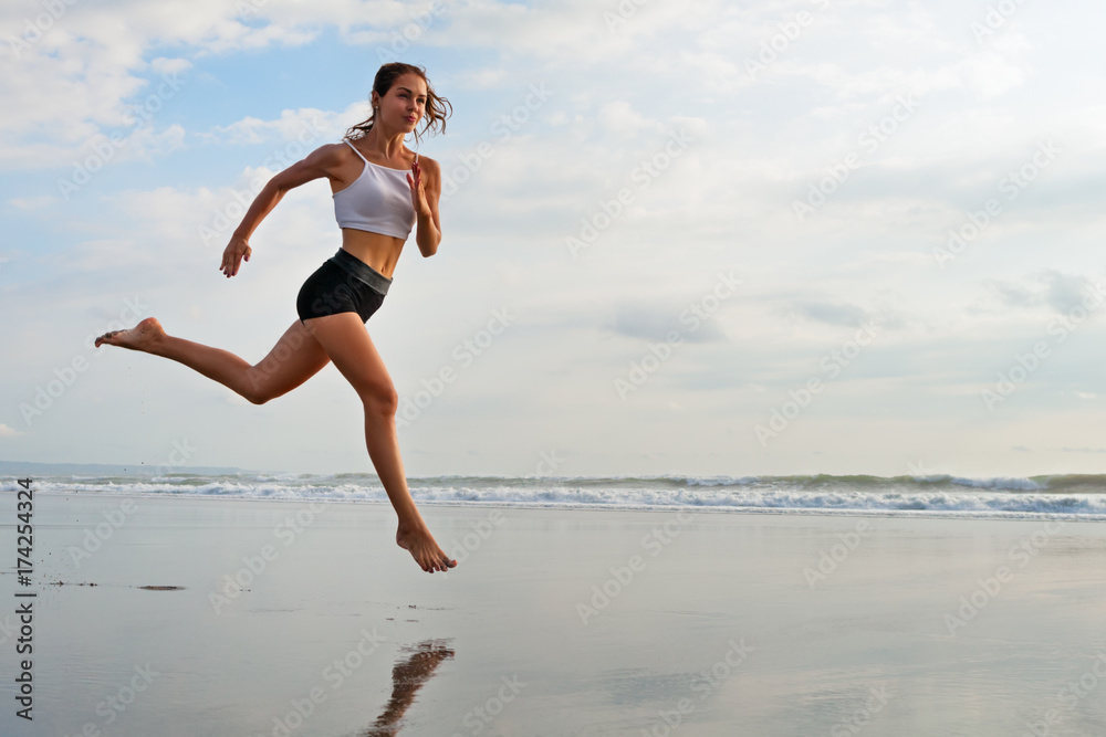 Barefoot sporty girl with slim body running along sea surf by water pool to keep fit and health. Bea