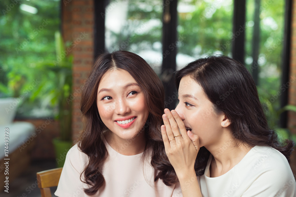 两个女孩在八卦。迷人的年轻女子在朋友耳边窃窃私语