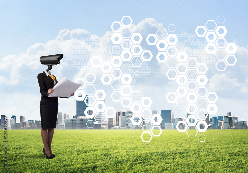 Camera headed woman standing on green grass against modern cityscape