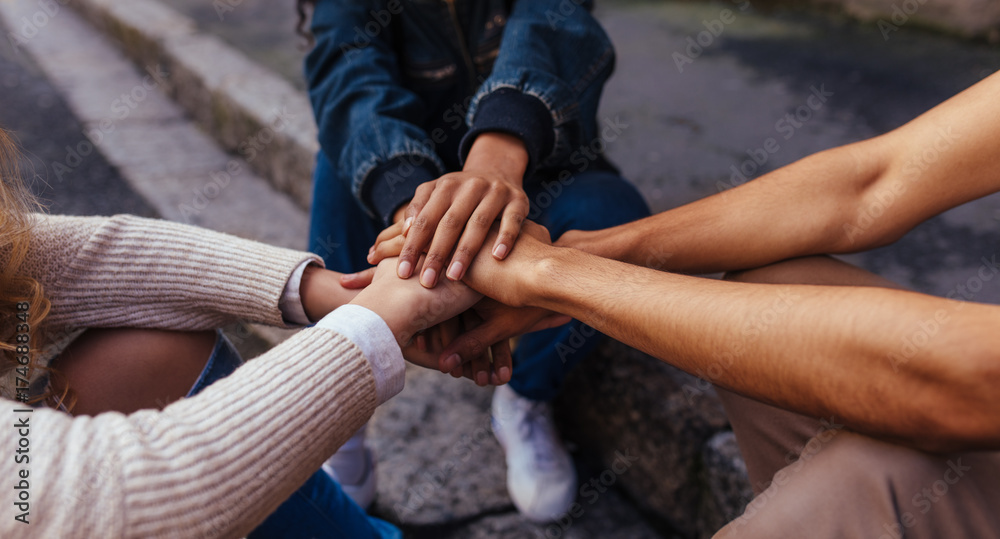 Group of friends sitting together stacking their hands on one an