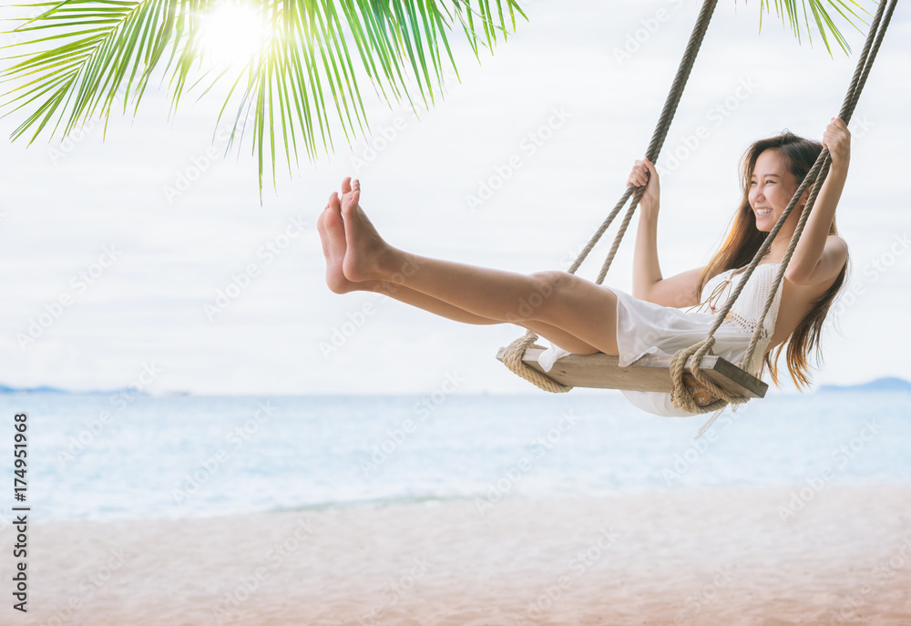 Asian lady relax and fun with swing under coconut leaves and sand beach