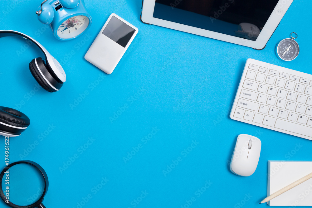 Blue office desk table with computer,wireless earphone,alarm clock and business objects, Top view wi