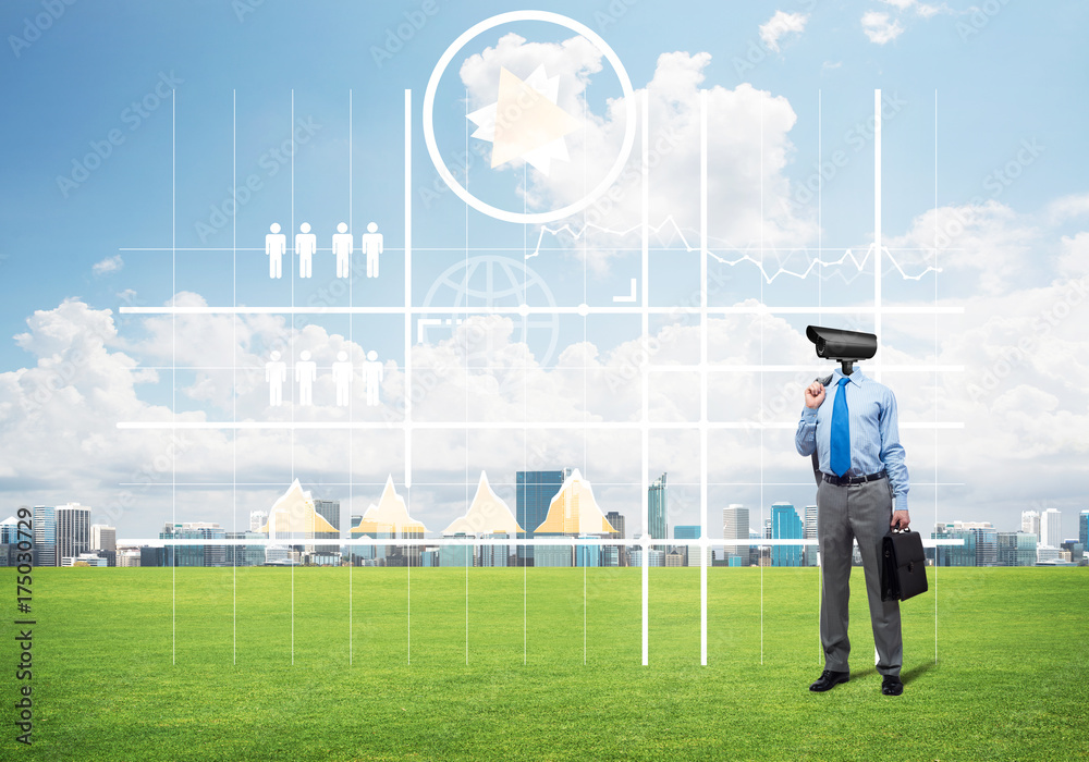 Camera headed man standing on green grass against modern cityscape