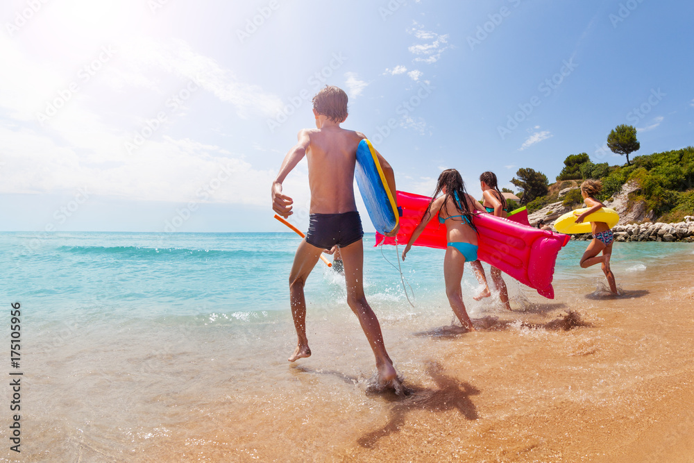 Group of kids run into the sea on sunny beach