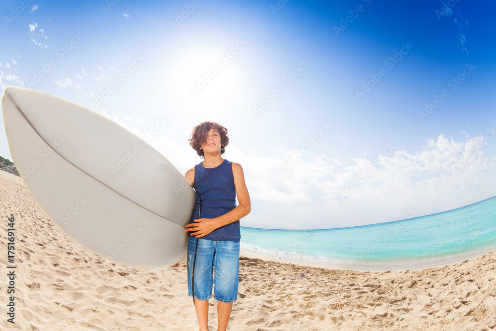 Happy kid standing on sandy beach with surf board