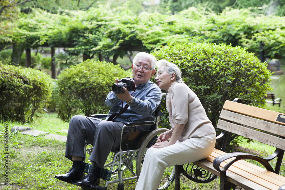 An old couple are taking pictures at a park bench