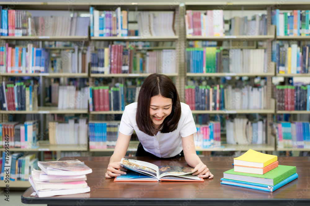 快乐的亚洲女学生在课间休息时在现代的书架旁看书