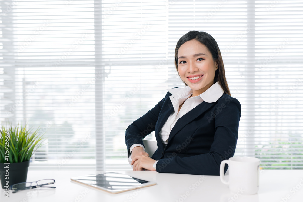 Confident asian businesswoman sitting by desk in office