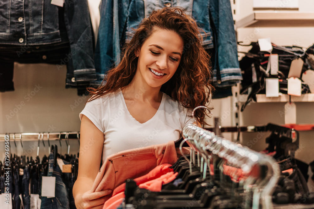 The attractive girl considers clothes in shop.