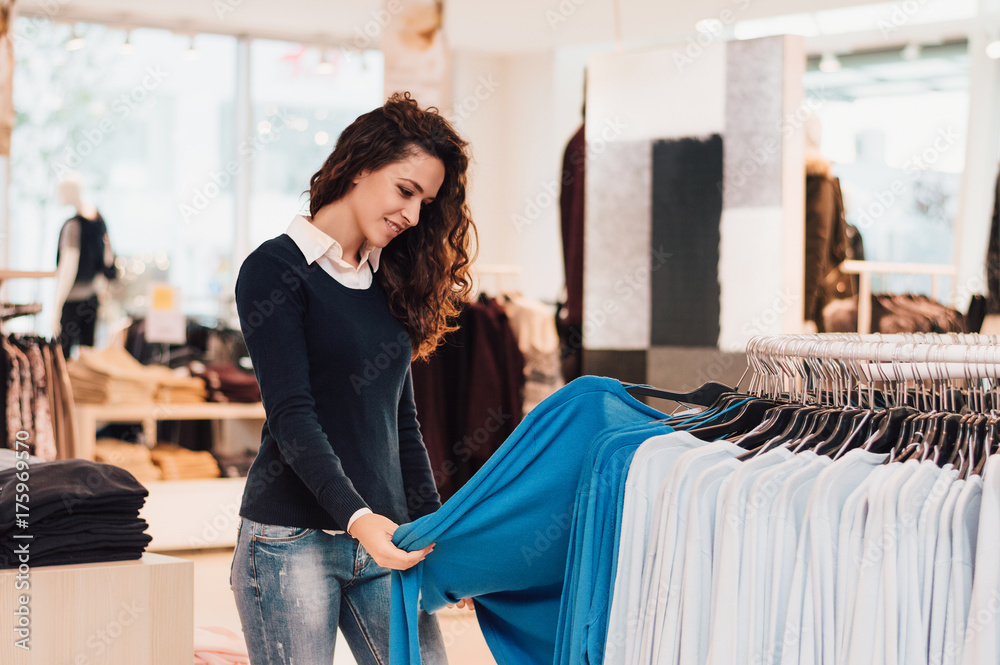 Happy young woman choosing clothes in mall or clothing store.