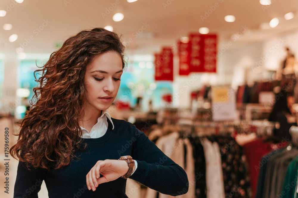 Portrait of brunette woman in shopping mall looking at watch.