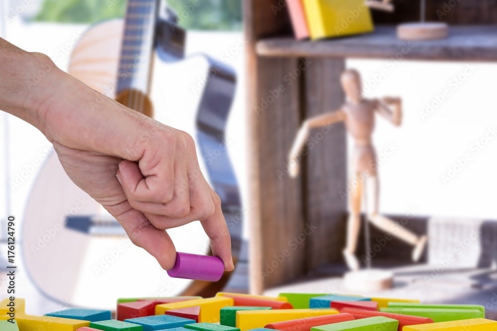 Composite image of cropped hand arranging plastic blocks