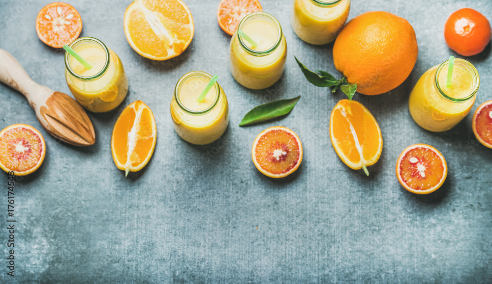 Healthy yellow smoothie with citrus fruit and ginger in bottles with straws over grey concrete backg