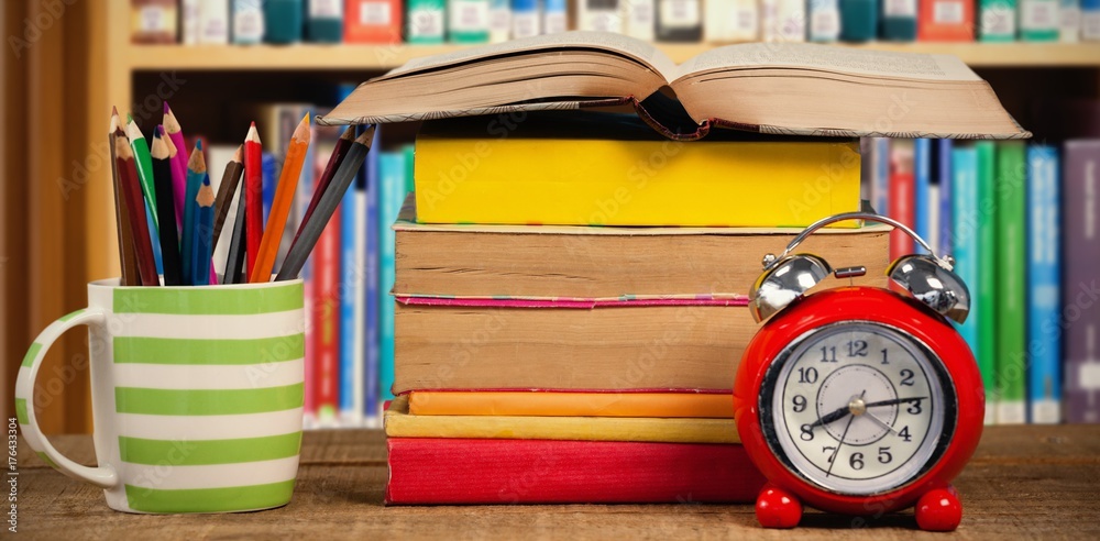 Composite image of stack of books by mug with colored pencils