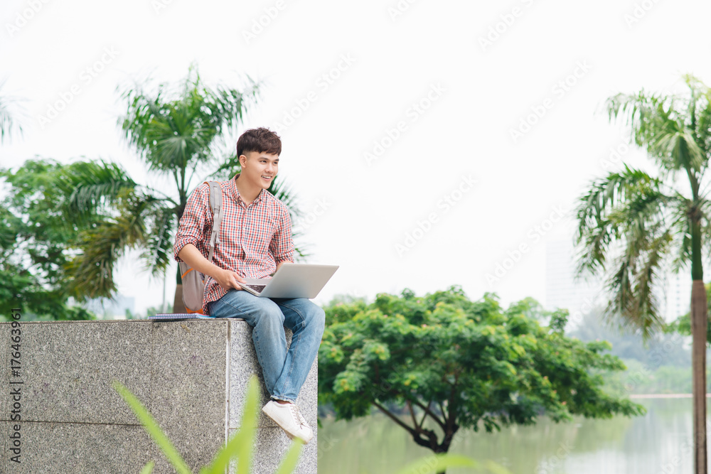 Young man sitting with laptop outside the university building