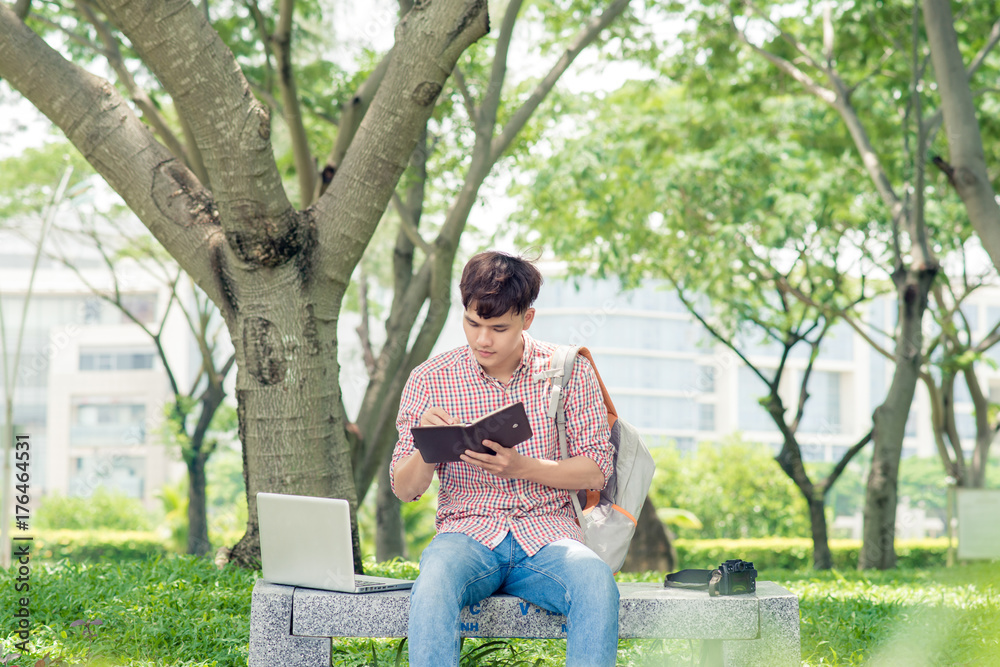 Asian student writing compositions in copybooks sitting in park