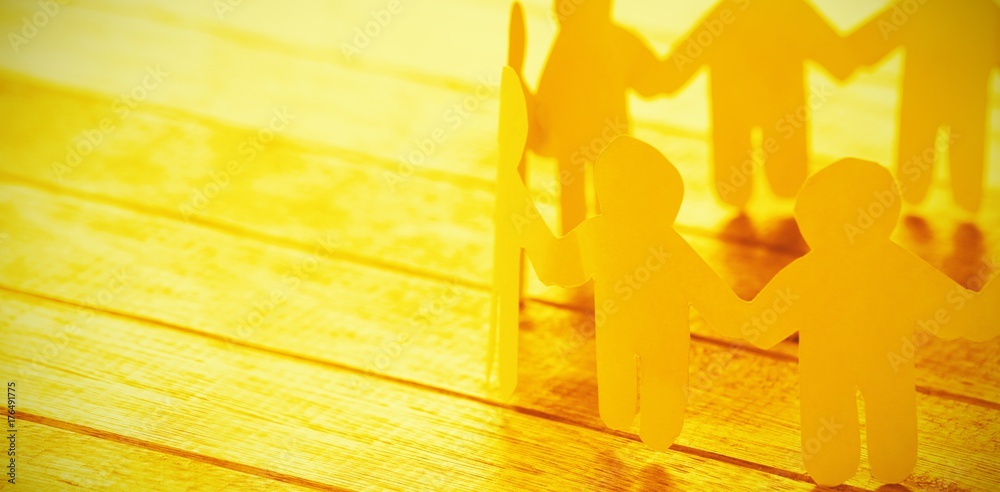 Yellow paper figures holding hands on wooden table