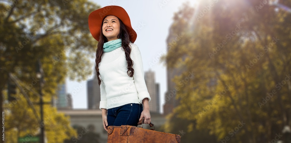 Composite image of asian woman with hat holding luggage 