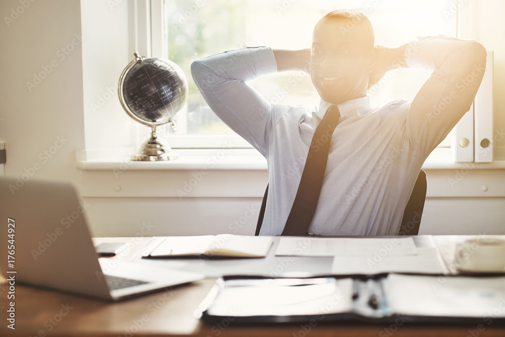 Content young businessman leaning back in his office chair