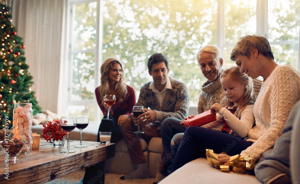 Little girl sitting with family and opening present