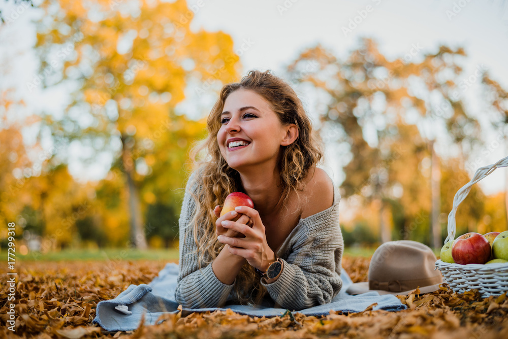 Young stylish woman laying down on the ground in autumn park.