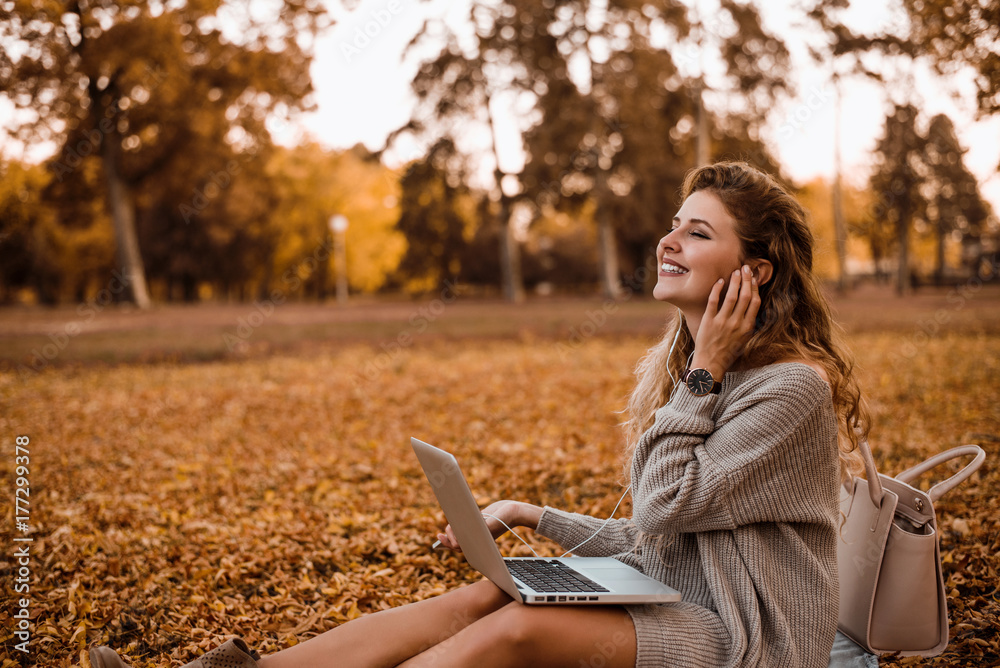 Young fashionable woman sitting in autumn park and talking on phone.