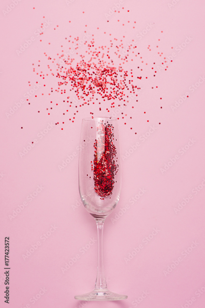 Flat lay of Celebration. Champagne glass with colorful party streamers on pink background.