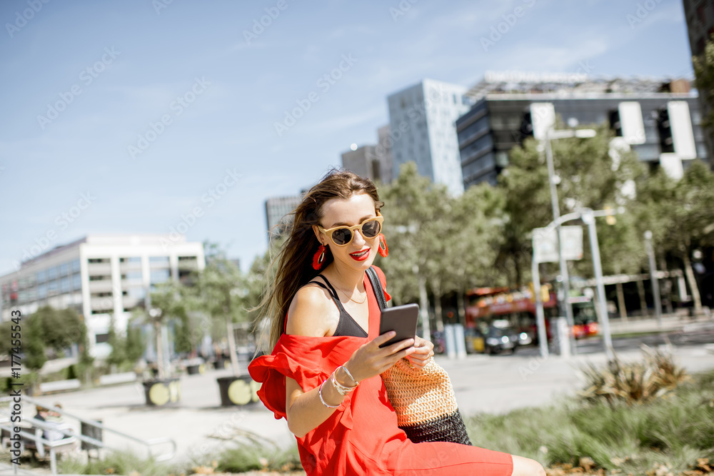 Lifestyle portrait of a business woman with phone in red dress sitting outdoors at the modern office